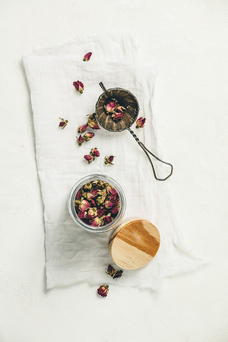 Dry rose buds tea in glass jar and tea strainer. Top view, flat lay