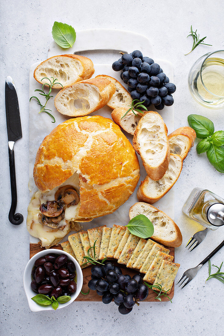 Baked brie wrapped in puff pastry with mushrooms with bread and cracker on a board