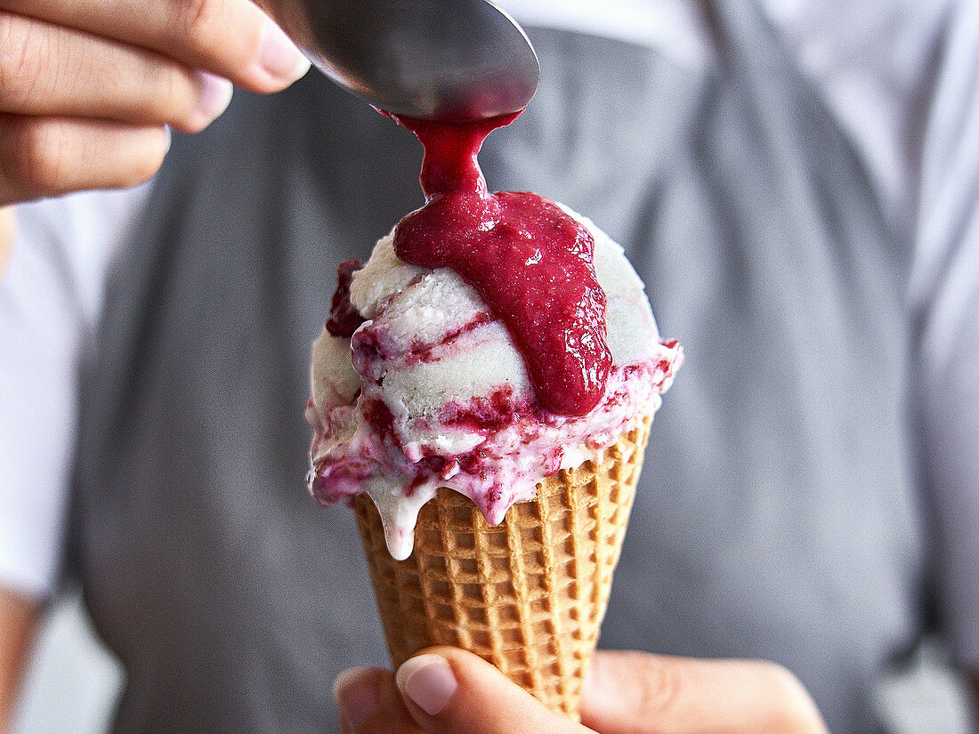 Skyr ice cream with cherry swirl and cherry sauce in a waffle cone