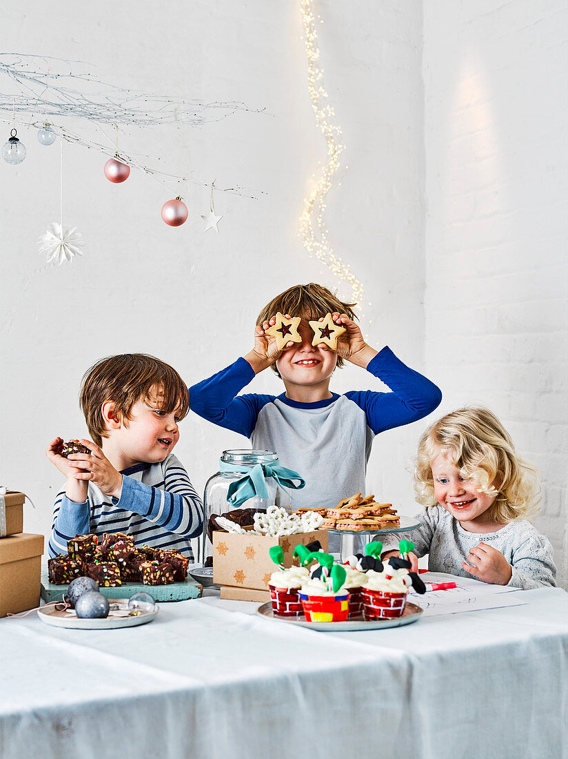 Drei Kinder um Weihnachtstisch mit selbstgemachtem Gebäck und Plätzchen