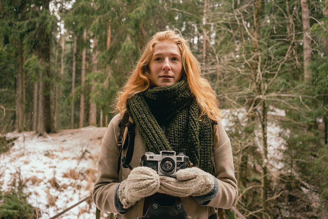 Rothaarige Frau mit Fotoapparat im verschneiten Wald