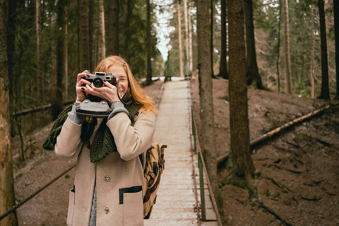 Frau fotografiert mit Retro-Fotoapparat auf Fußgängerbrücke im Wald