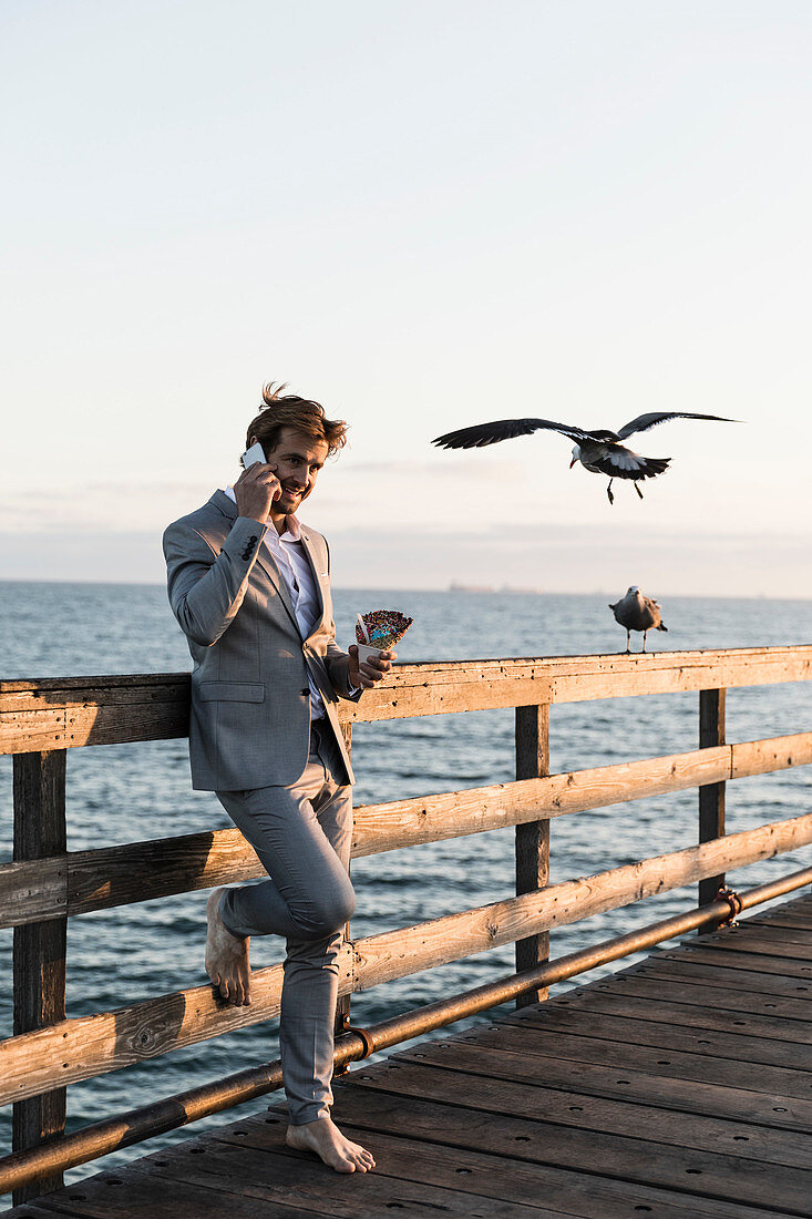 Geschäftsmann barfuß telefoniert mit einem Smartphone am sonnigen Pier, Los Angeles, Kalifornien