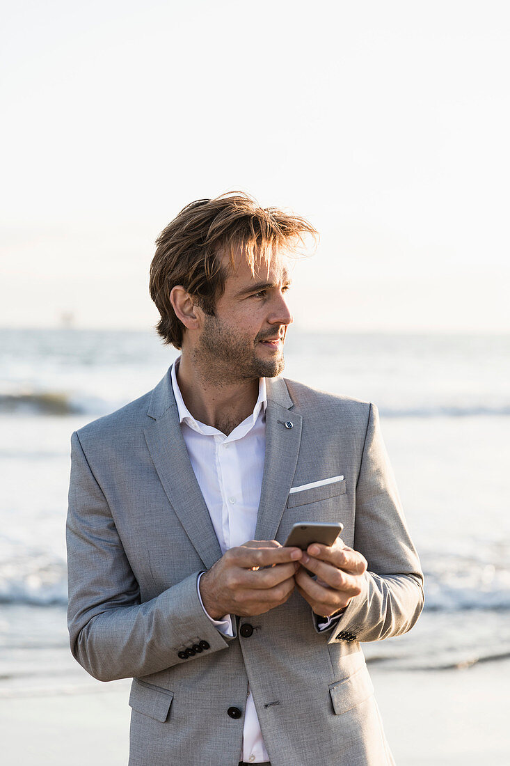 Geschäftsmann mit Smartphone am Strand am Ozean