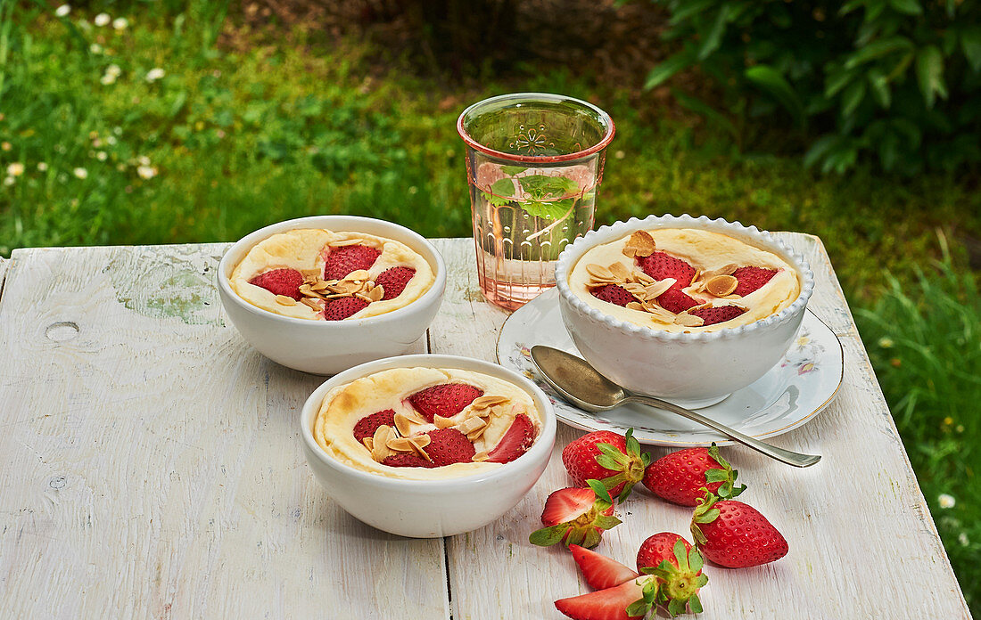 Überbackener Hüttenkäse mit Erdbeeren in Schälchen auf Tisch im Freien