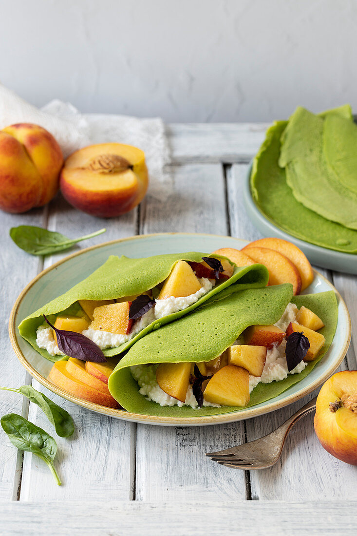 Green spinach crepes with cottage cheese and fresh peaches