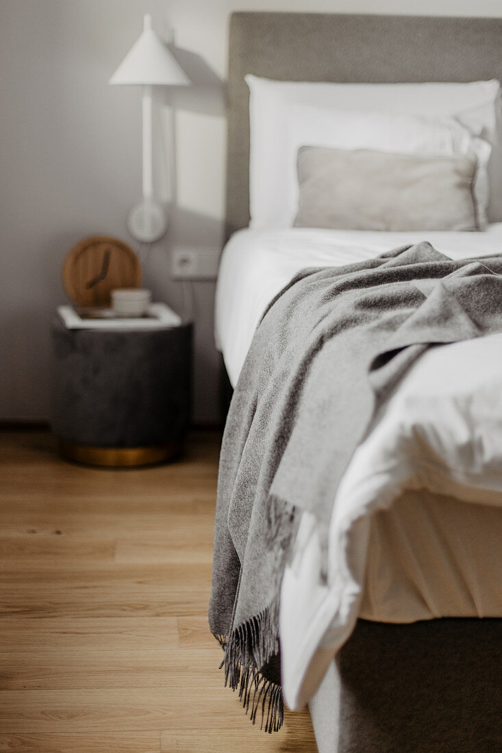 Bedside table and wall-mounted lamp next to bed with white bed linen