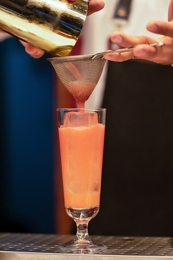 Barkeeper giesst Cocktail durch Barsieb in Glas