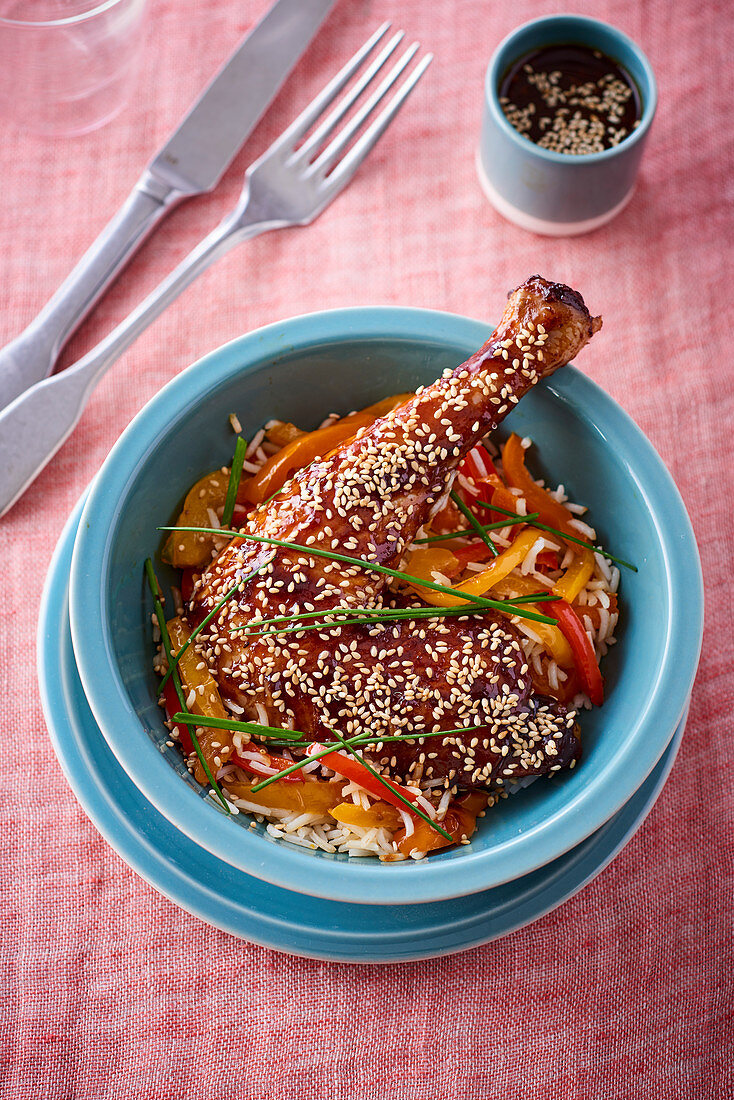 Glazed chicken leg with sesame seeds on a pepper medley and rice