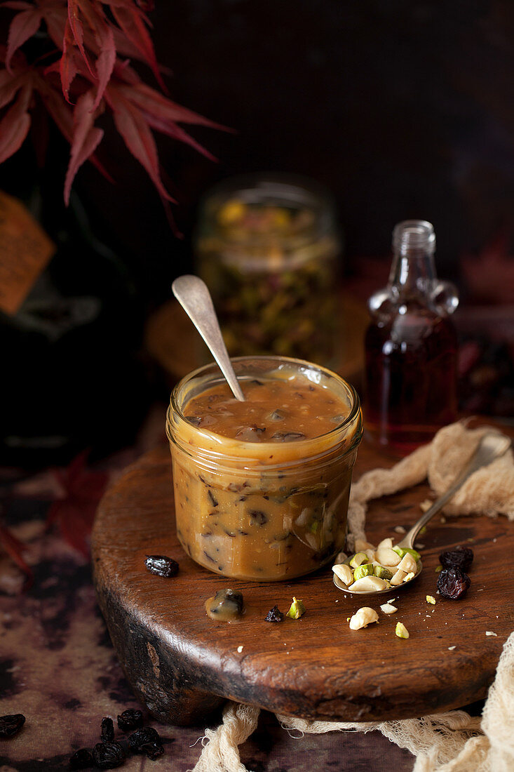Glass jar of caramel sauce with dried fruit and nuts mixed in and alongside the jar