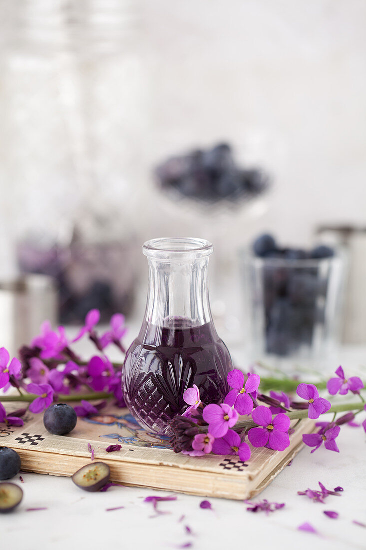 Small vintage bottle of violet liqueur surrounding by purple flowers