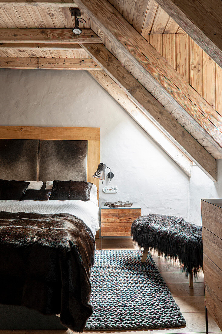 Luxuriöses Doppelbett und Hocker mit Tierfell im Schlafzimmer mit Holzdecke und Fenster