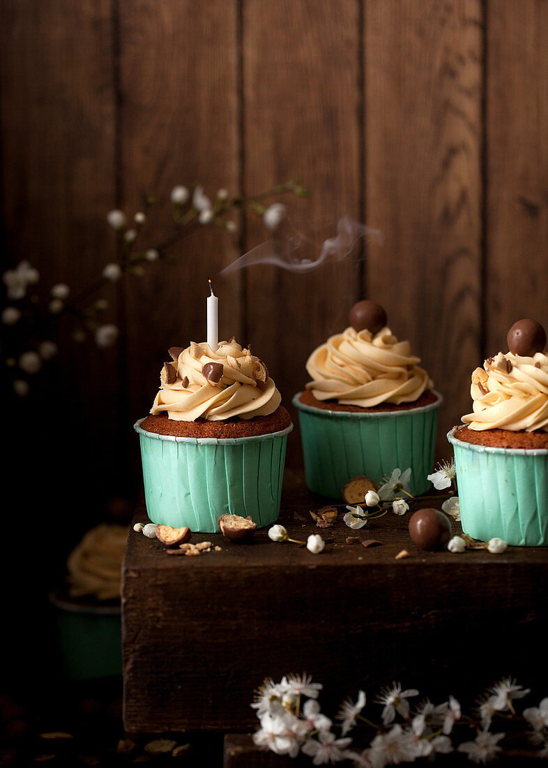 Cupcakes decorated with buttercream and chocolate malt balls, one with a smoking candle