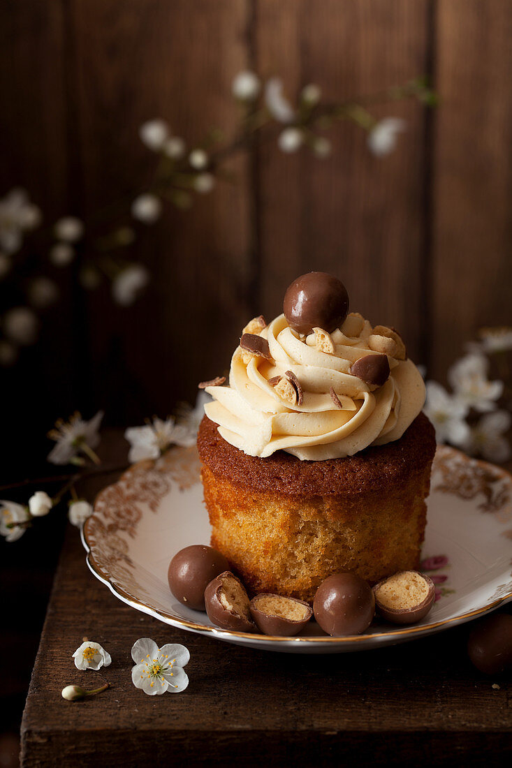 Cupcake out of its wrapper decorated with piped buttercream and chocolate malt balls