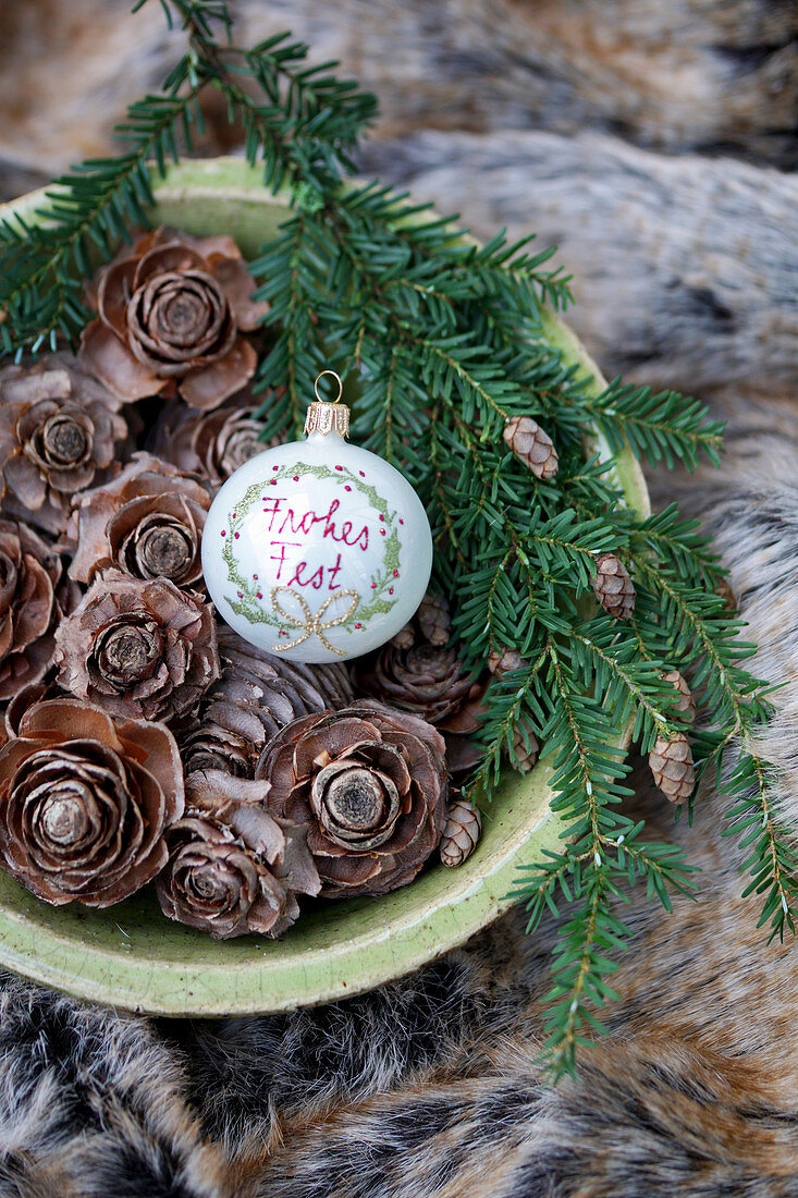 Bauble with Christmas greeting and larch cones in bowl