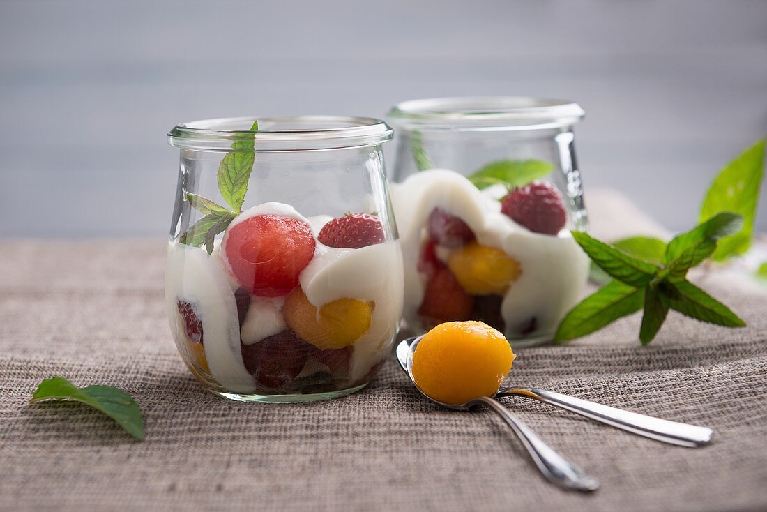 Sojajoghurt mit Melonen-und Pfirsich-Kugeln, Erdbeeren und roten Trauben