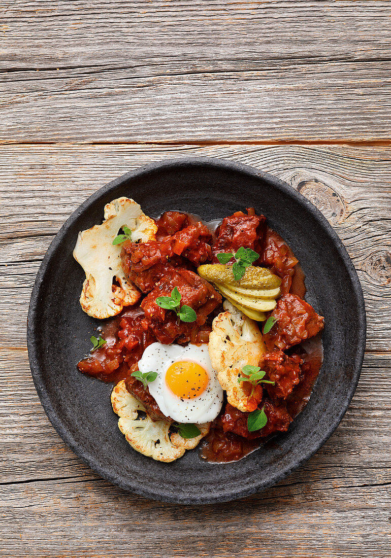 Fiakergulasch (Viennese-style goulash with beef topped with sausage, fried egg and gherkins) with cauliflower and a quail's egg