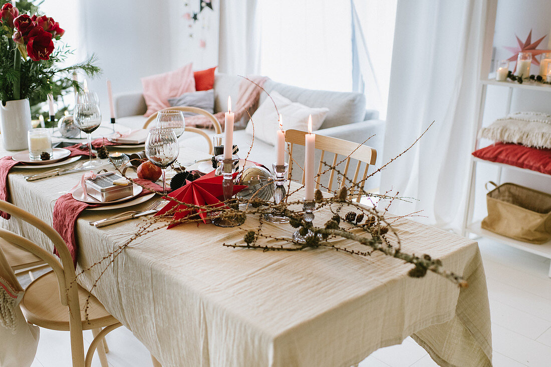 Table set for Christmas meal with red paper star, larch branches and vase of amaryllis