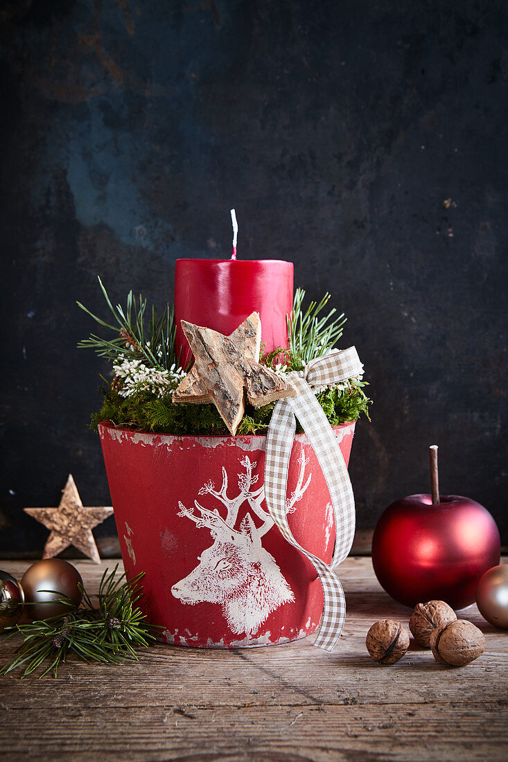 Festive arrangement with red candle in flower pot decorated with white stag's head