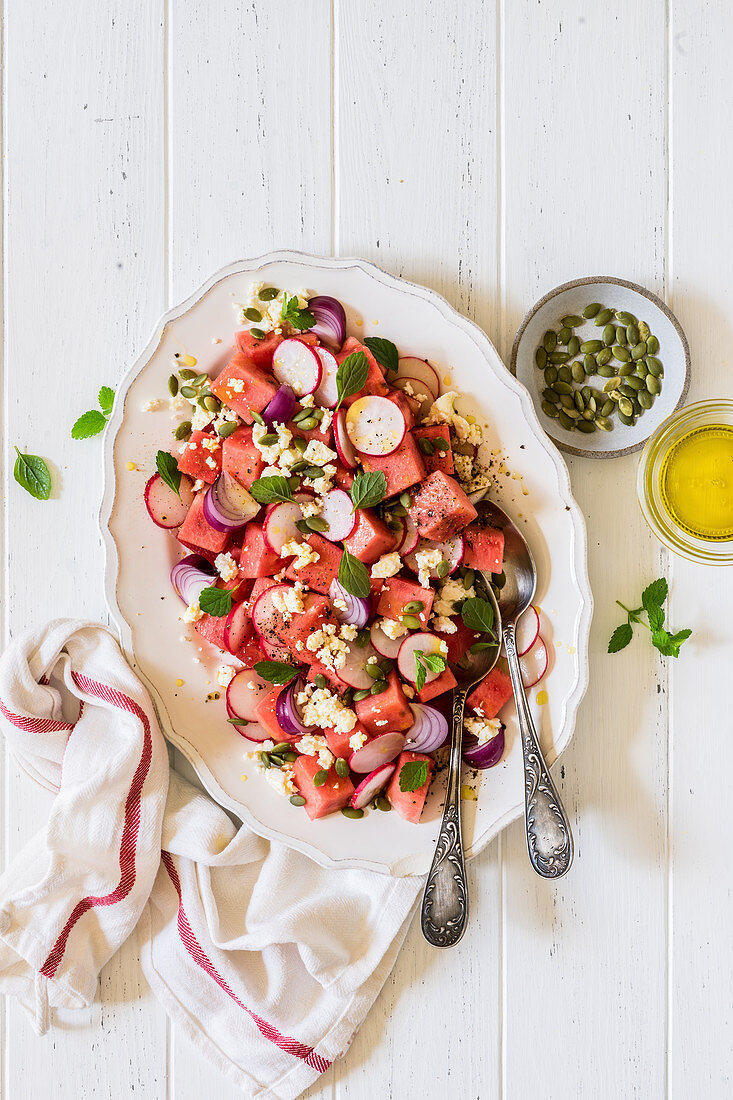 Salat aus Wassermelone, Radieschen, Feta, roten Zwiebeln und Kürbiskernen