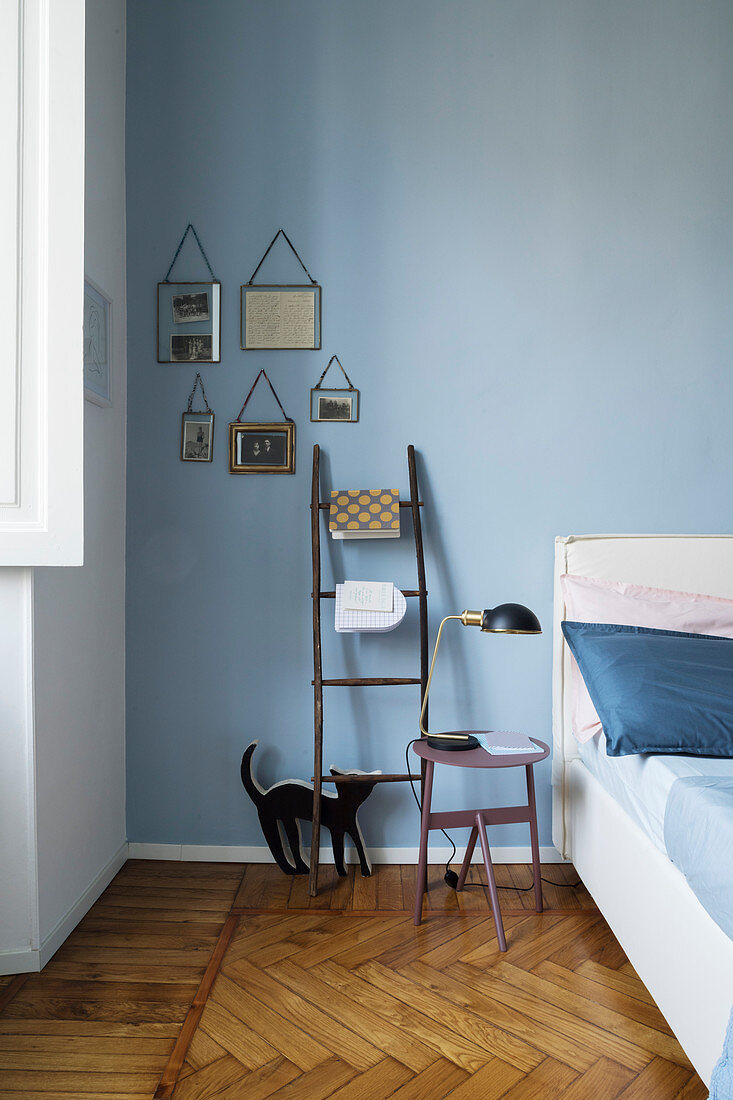 Ladder used as shelf and bedside table against blue wall in bedroom