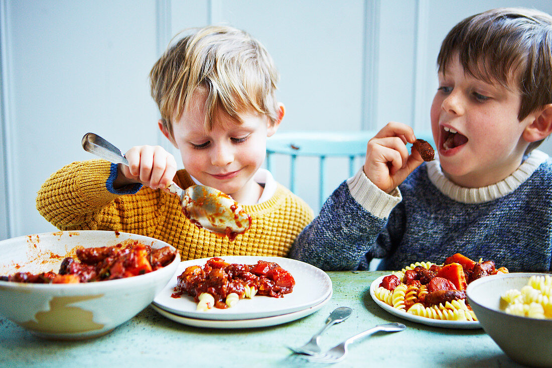Zwei Jungen essen Wursteintopf (Slow Cooking) mit Spiralnudeln