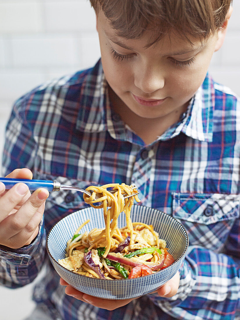 Boy eating noodle stir-fry with crunchy peanuts