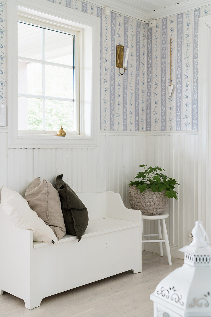 Sitzbank im Vorraum mit weißer, halbhoher Holzverkleidung und romantischer Tapete