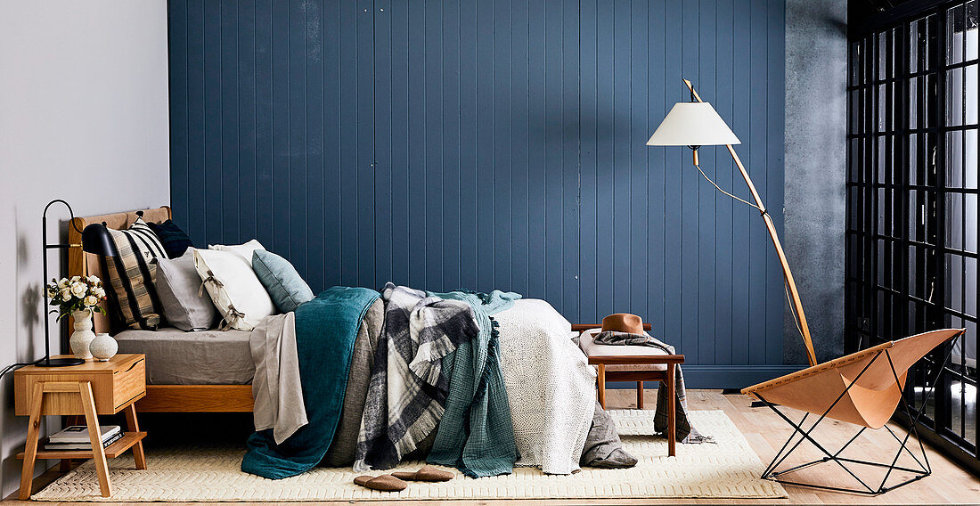 Bed in layered look in front of blue board wall in bedroom