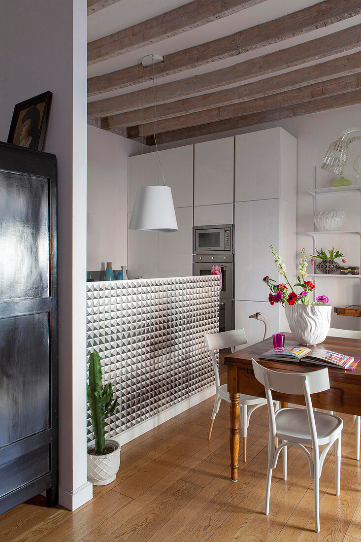 Old wooden table next to white, modern kitchen in open-plan interior