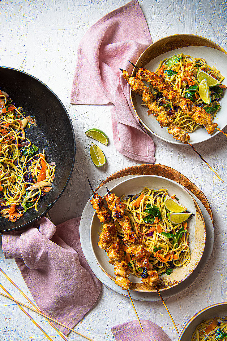Chicken satay skewers with stir fry vegetable noodles and lime wedges