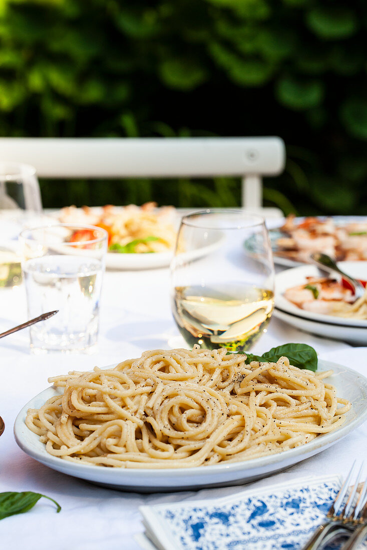 Platter of cacio e pepe (pasta with cheese and pepper) with basil, and shrimp skewers on an outdoor table