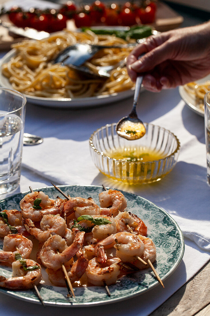 Shrimp skewers with basil butter sauce, pasta cacio e pepe (pasta with cheese and pepper) and tomatoes on an outdoor table