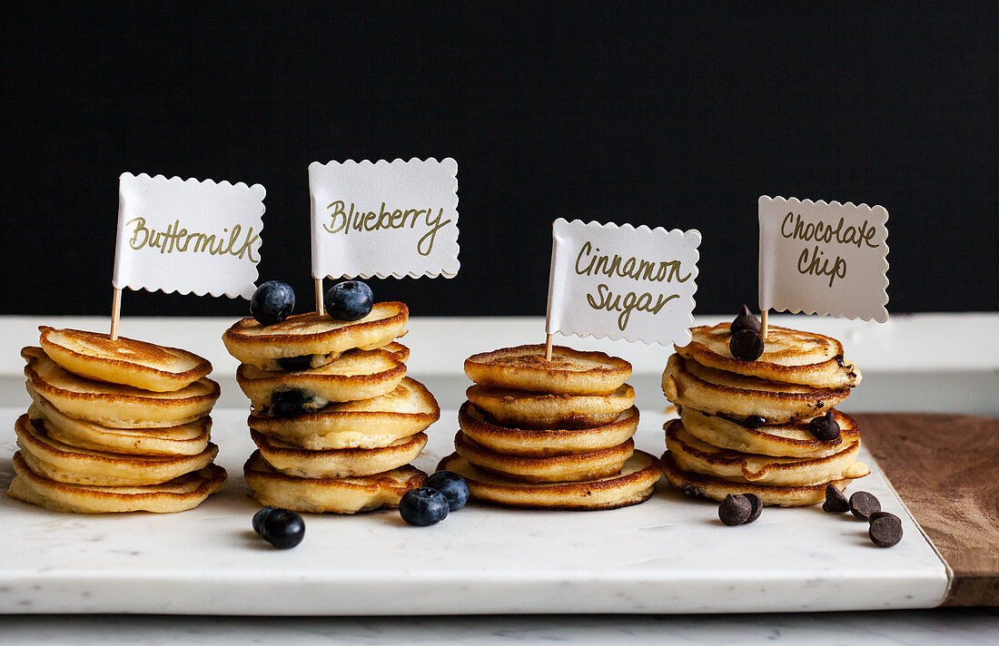 Stacks of mini pancakes with signs, fruit and chocolate chips, on a marble board