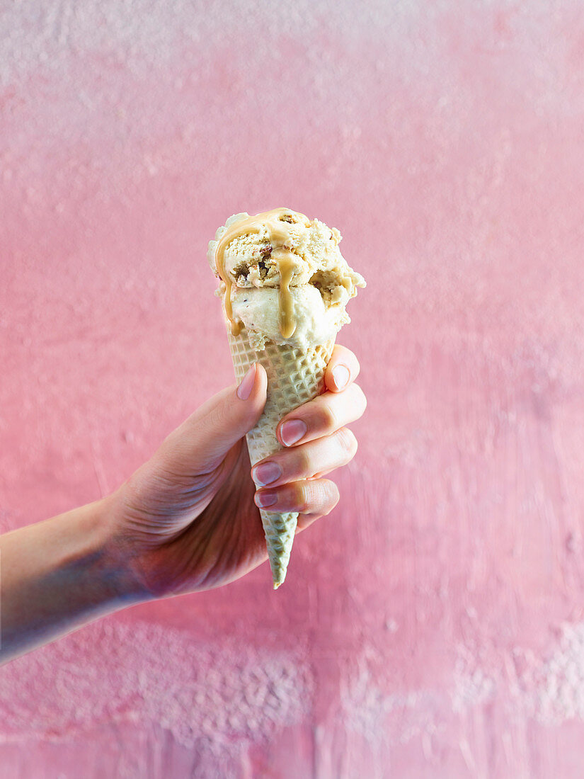 Hand hält Eistüte mit Kokos-Karamell-Pekannuss-Eis