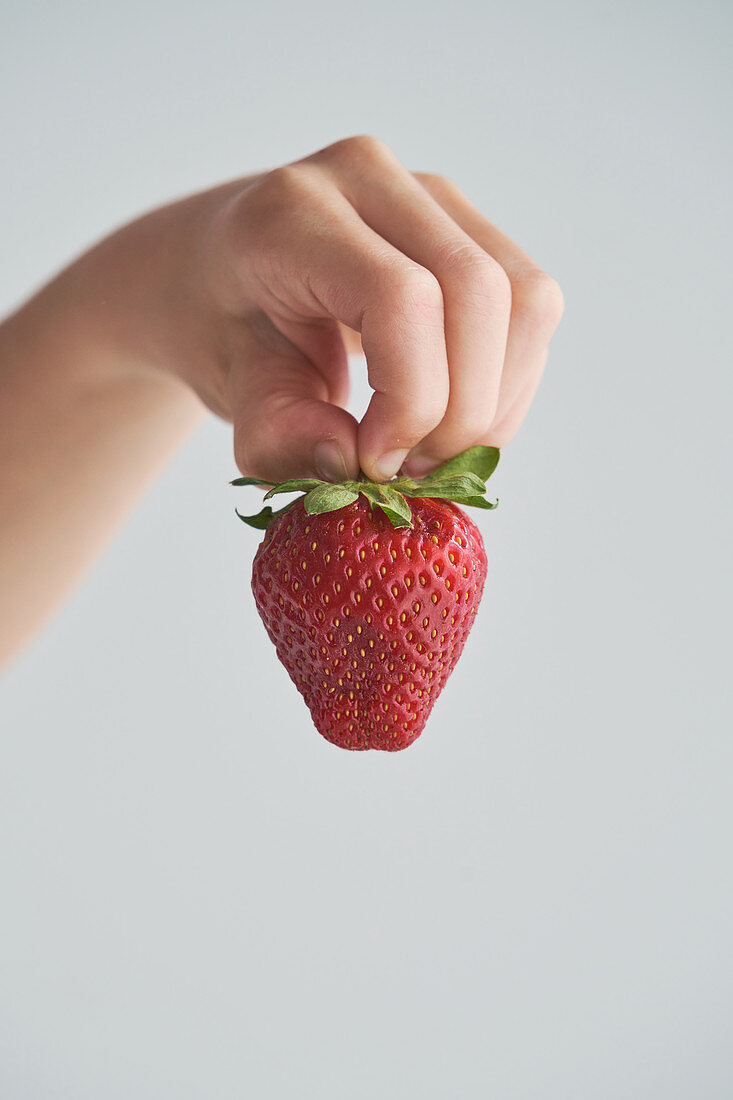 Cropped anonymous kid demonstrating fresh strawberries on his hand on blurred background