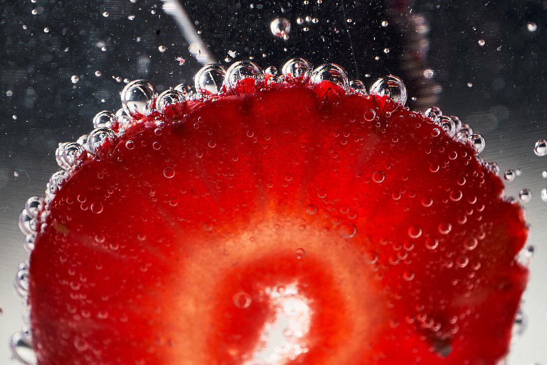 Closeup ripe red sliced strawberry covered with air bubbles floating in transparent clear water