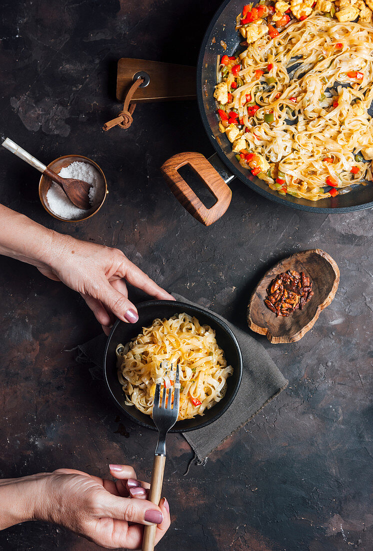 Female hand with fork and bowl of tasty spicy rice noodles with chicken and vegetables served for dinner