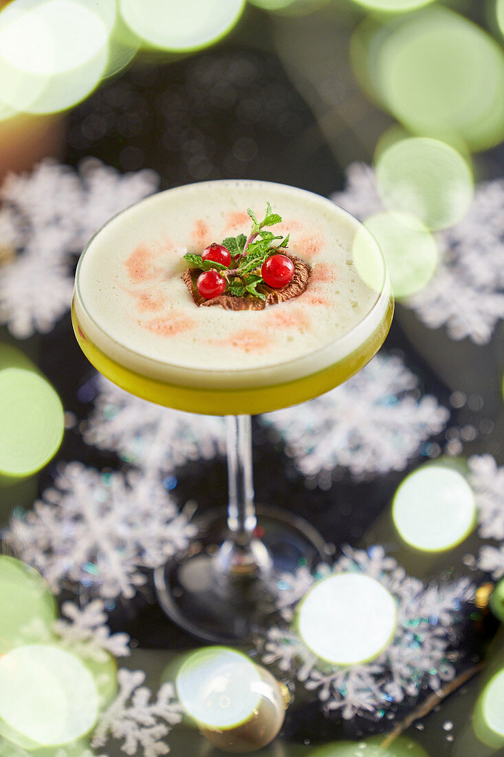 Round glass of mezcal cocktail with kiwi and maple syrup with table decorated with snow stars