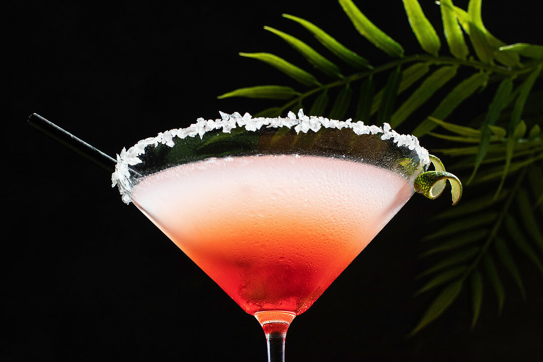 Tropical Margarita Cocktail with Grenadine placed on glittery table with plant leaves on black background