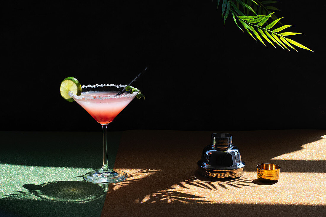 Tropical Margarita Cocktail with Grenadine placed on glittery table with plant leaves on black background