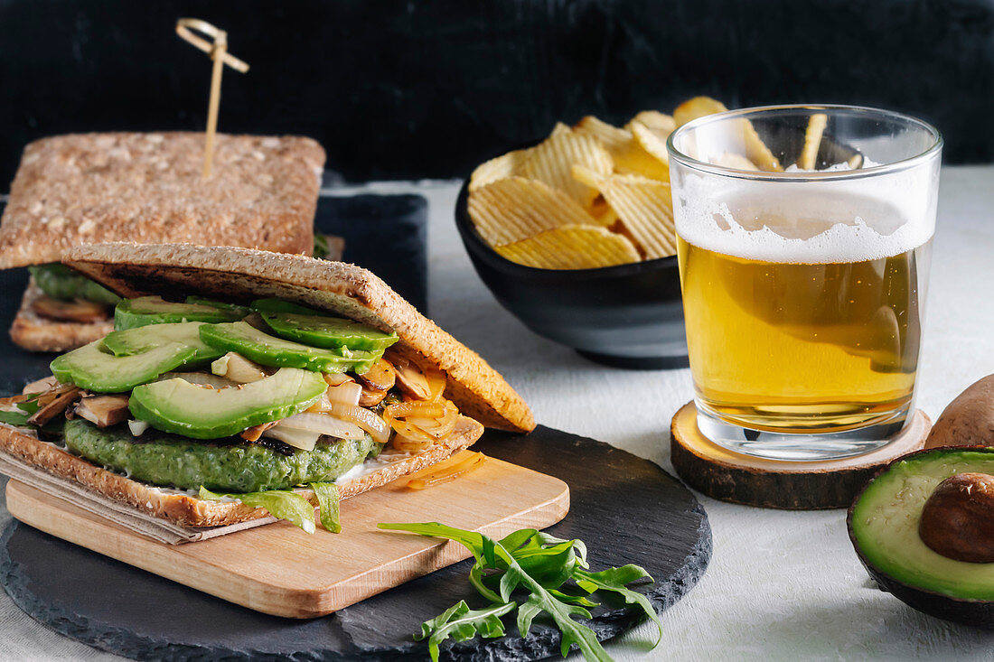 Tasty sandwich with avocado placed on table with glass of beer and potato chips in cafe