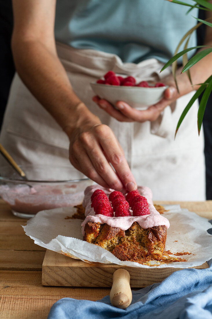 Crop anonymous female with homemade cake with glaze and fresh raspberries in home kitchen