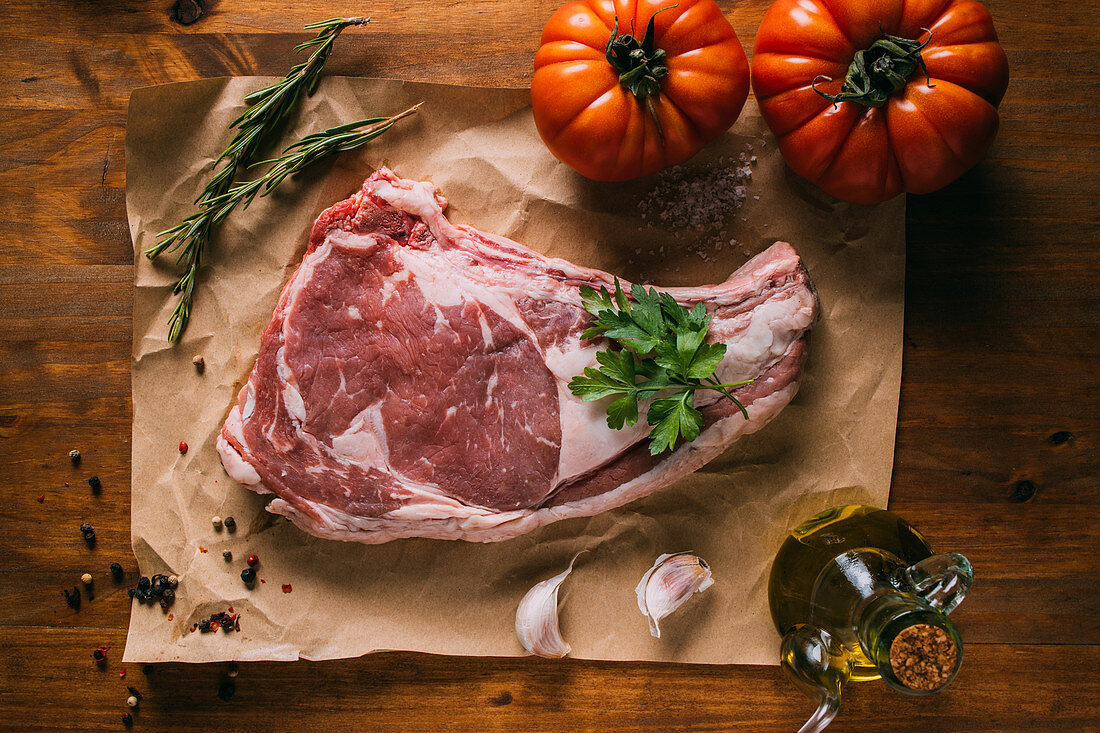 Rohes Rindersteak auf Papier mit Olivenöl, Tomaten, Gewürzen, Kräutern und Knoblauch