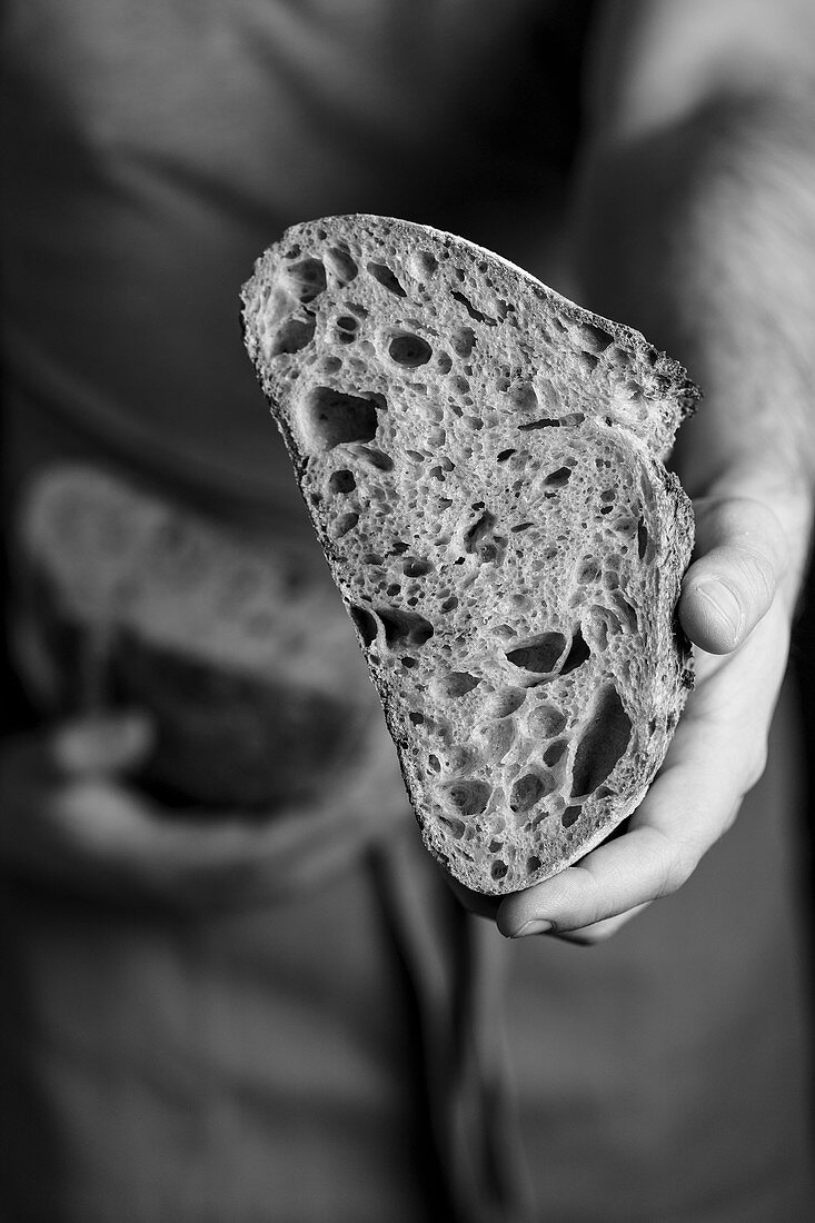 Crop male baker in apron holding cut in half loaf of fresh healthy artisan bread