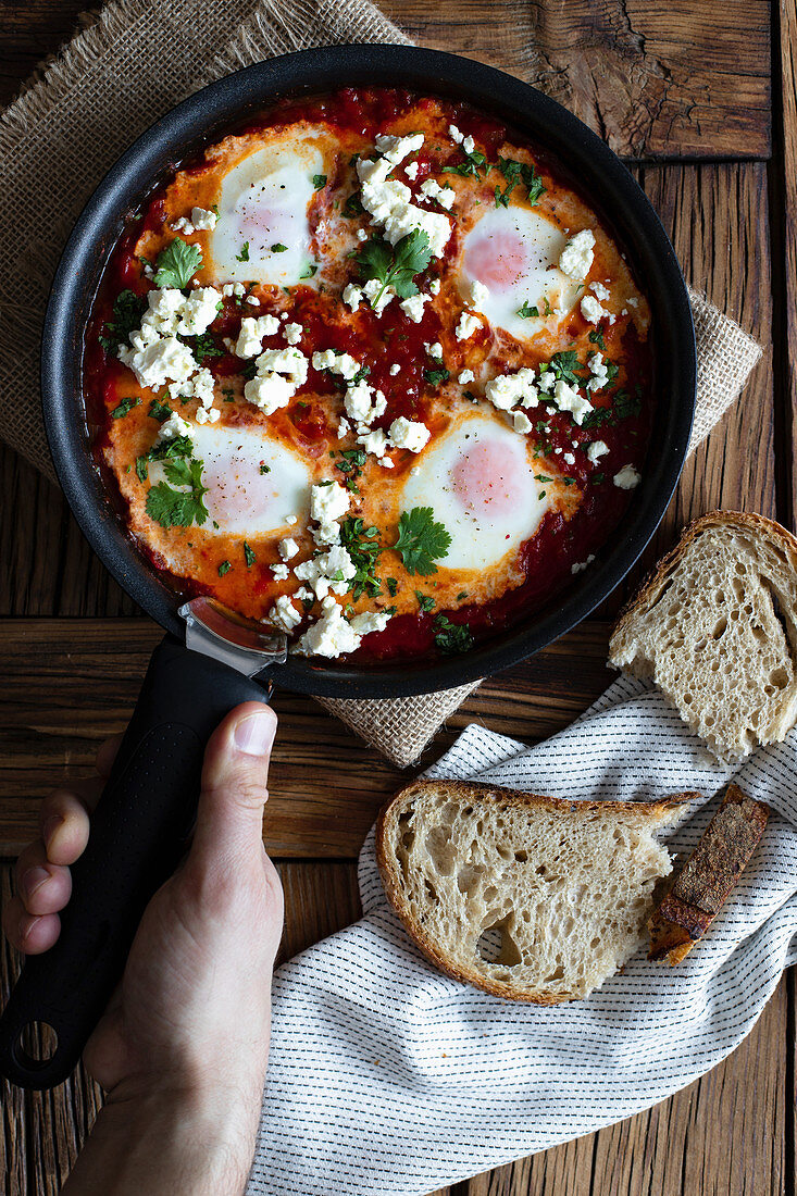 Frying pan with delicious shakshuka made with fried eggs with vegetables and feta cheese