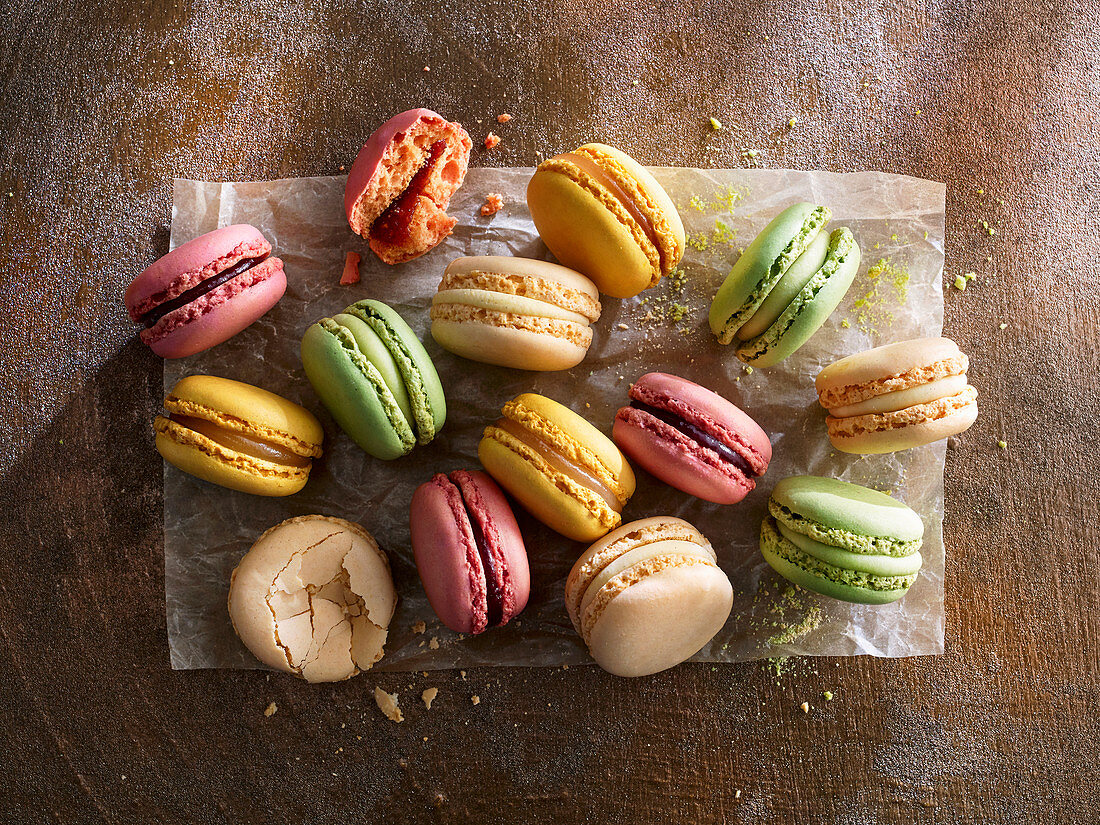 Different colorful macarons on paper against a wooden background