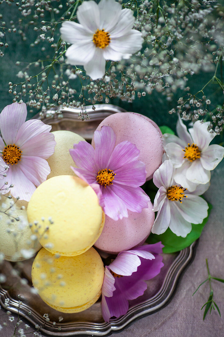 Different colored macarons decorated with flowers on a silver plate