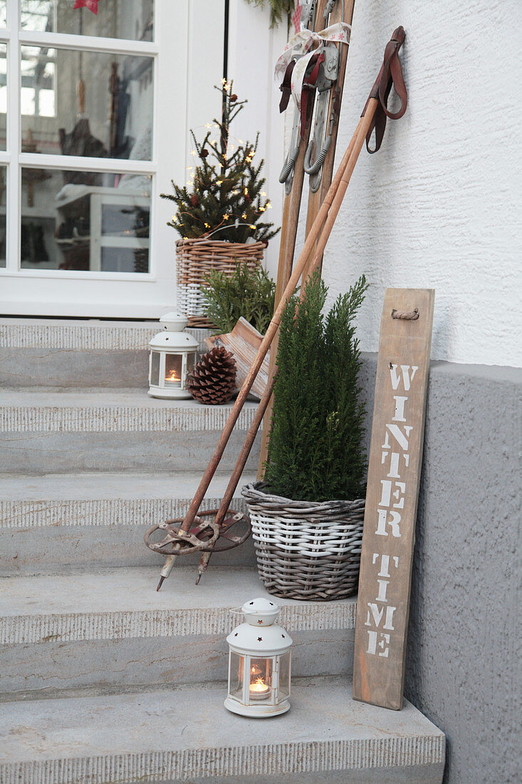 Winterliche Deko auf der Treppe mit alten Skiern, Skistöcken, Laternen und Bäumchen