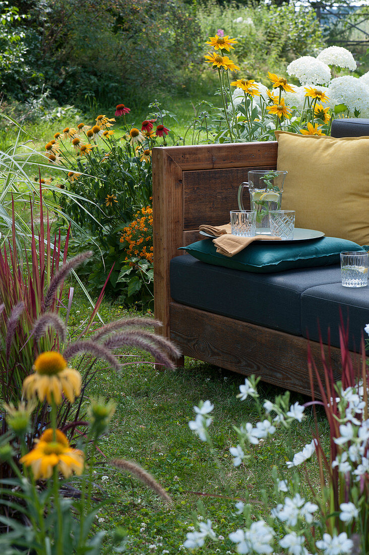 Sofa in the garden for living outside in summer, surrounded by Rudbeckia, hydrangeas shrub and grasses